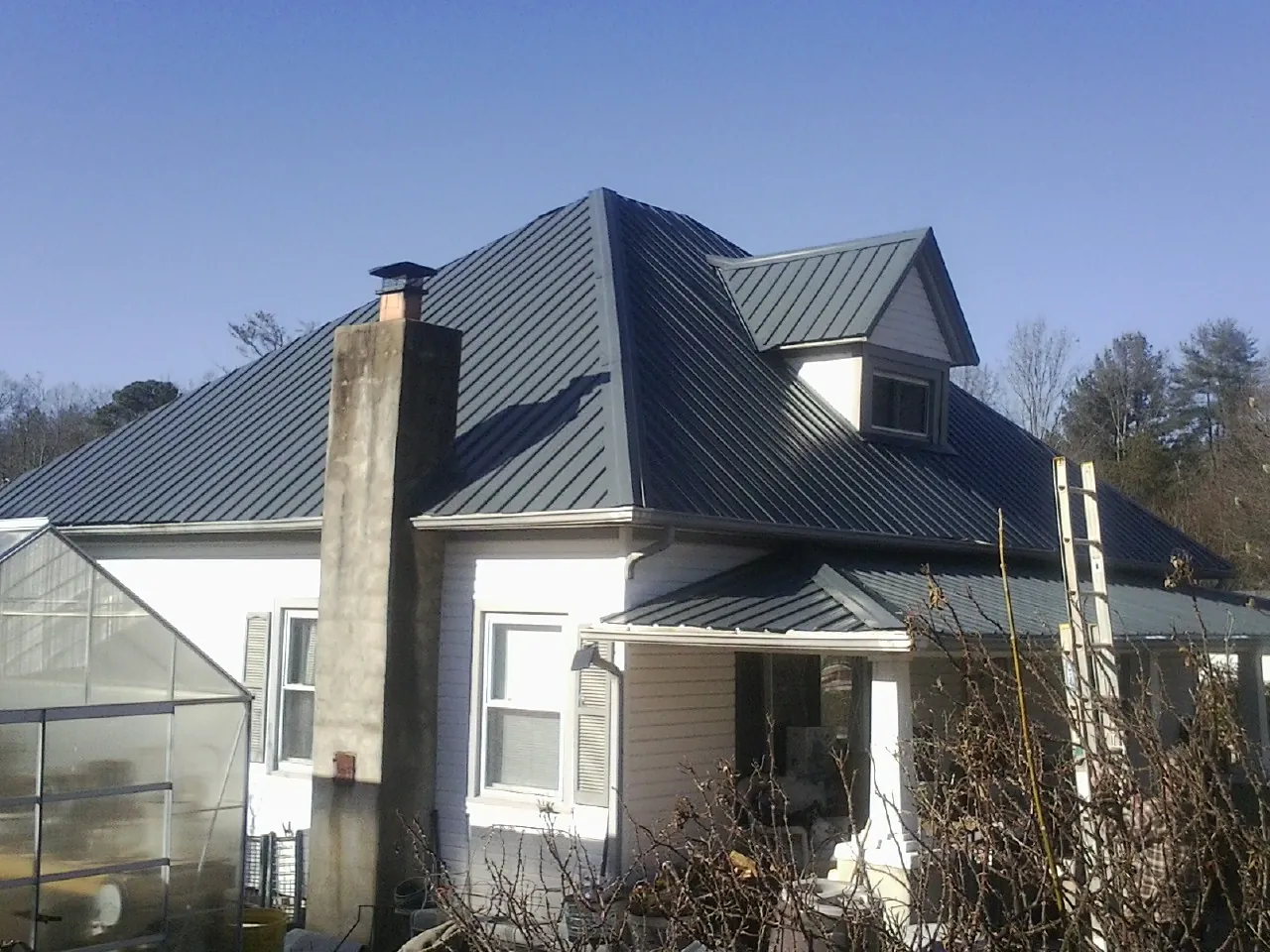 Dark blue standing seam metal roof on a white farmhouse with dormer — Slate & Tile Roof Repair by Roofing Brothers in Lee Center
