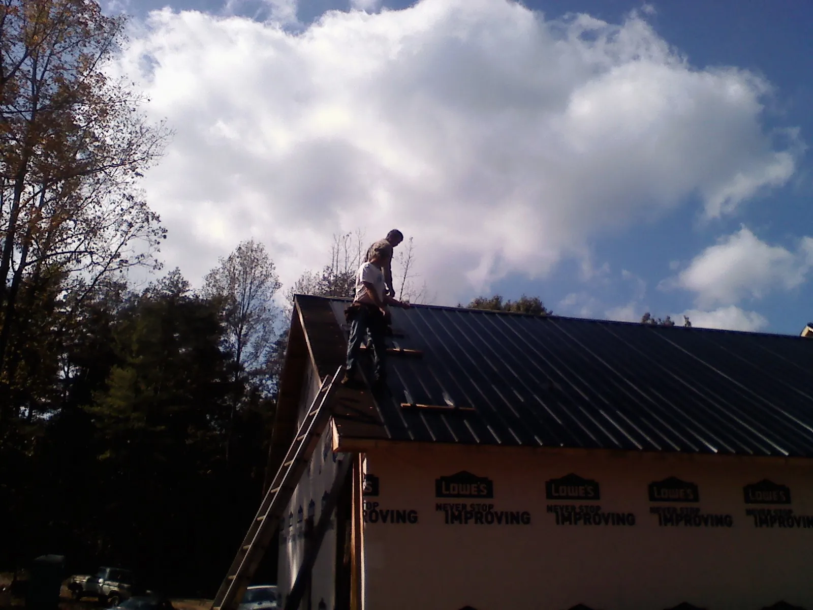Roofer fastening dark metal panels high against a cloudy sky, from a Roof Inspection job in Lee Center