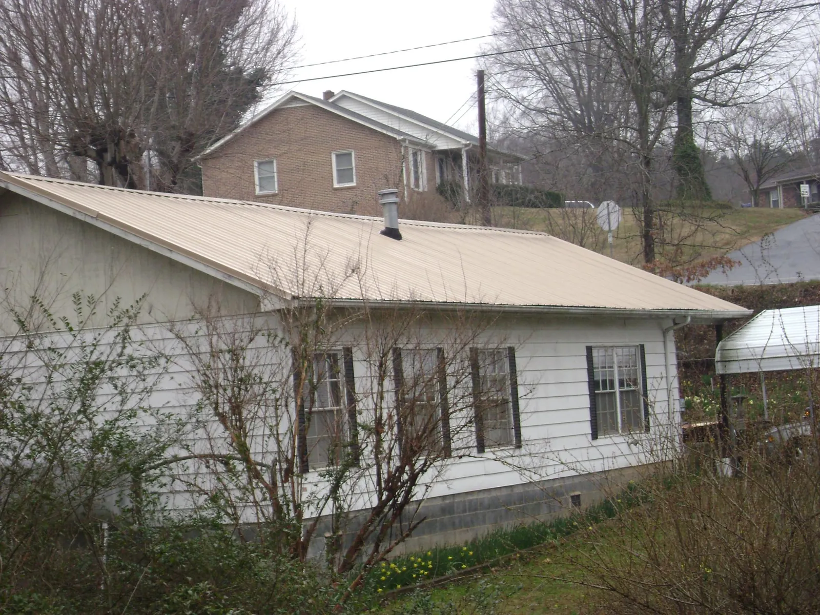 Tan metal roof on a white sided house set into a hillside — Commercial Roofing by Roofing Brothers in Lee Center